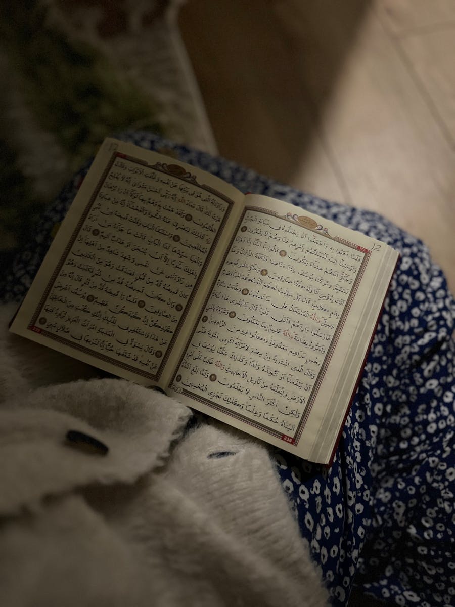 An open Quran on a lap with a blue floral background, highlighting Islamic culture.