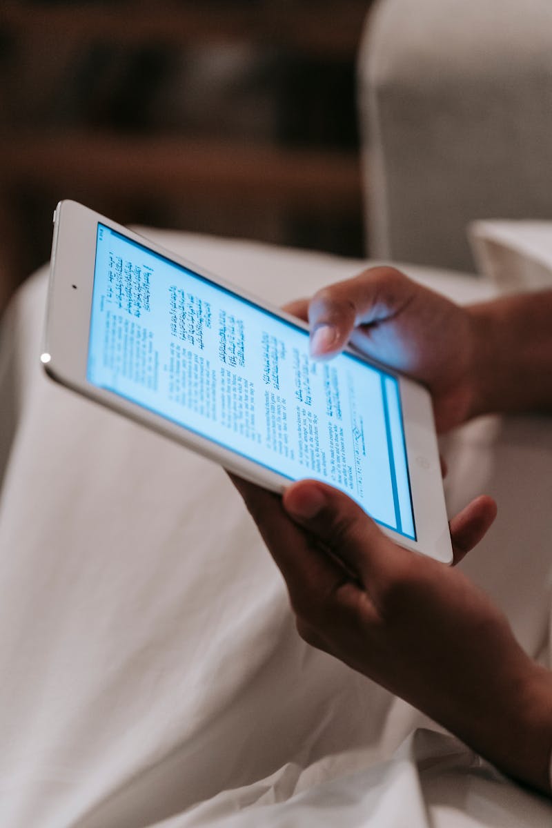 A person reading text on a digital tablet screen indoors, focusing on technology and modern reading habits.